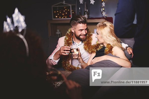 Man and woman at party  sitting on sofa  holding drinks  making a toast