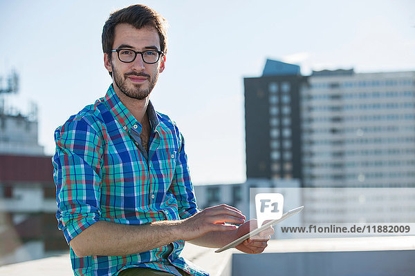 Porträt eines Mannes der neben einem Bürofenster steht und ein digitales Tablett benutzt