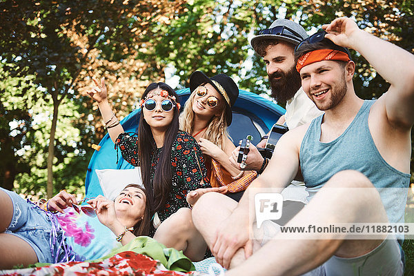Fünf junge erwachsene Freunde spielen Akustikgitarre beim Festival-Camping