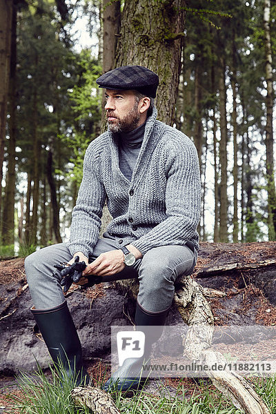 Man in outdoor clothes looking out from woodland log