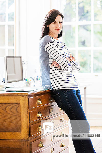 Portrait of female designer leaning against drawers in creative studio
