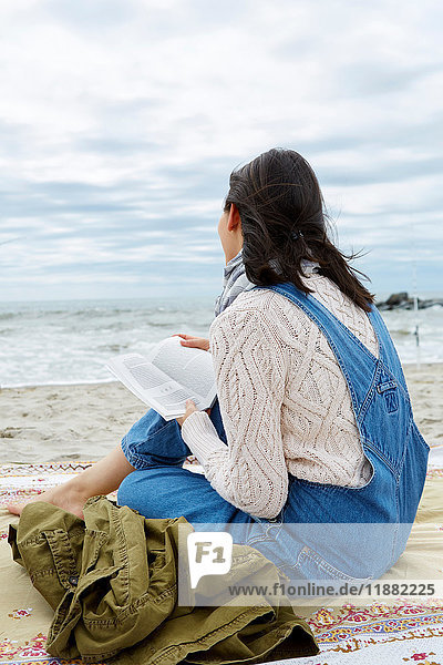 Junge Frau sitzt am Strand und schaut aufs Meer