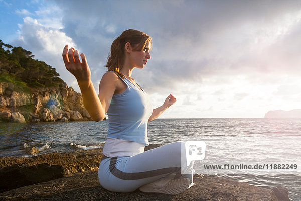 Woman sitting on rocks by sea meditating  Palma de Mallorca  Islas Baleares  Spain  Europe