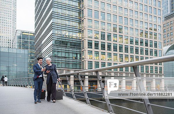 Businessman and businesswoman using mobile phone and pulling trolley luggage  Canary Wharf  London  UK