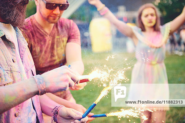 Young men covered in coloured chalk powder holding sparklers at festival