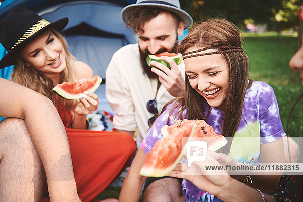 Young boho adult friends eating melon slices at festival