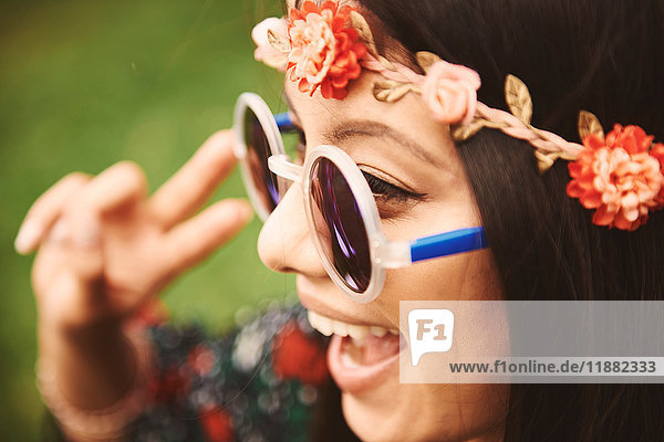 Young hippy woman in floral headband making peace sign at festival