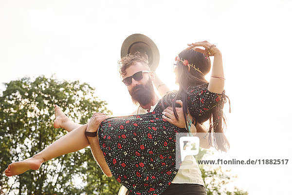 Junger Mann trägt Boho-Freundin auf dem Festival im Arm