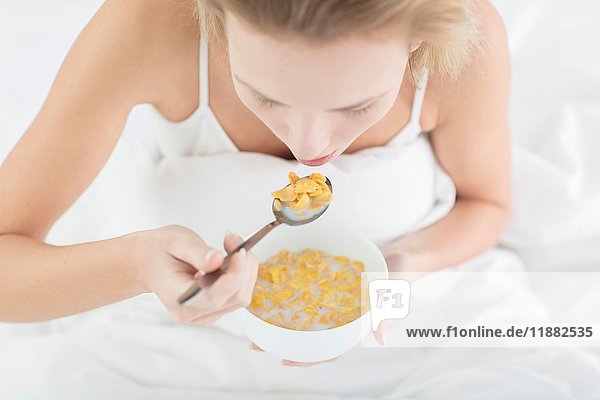 Junge Frau sitzt im Bett  isst Getreideschale  erhöhte Ansicht
