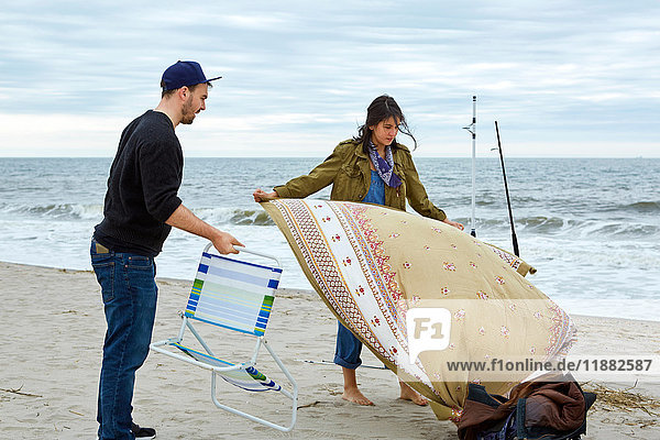 Junges Meeresfischerpaar bereitet Strandkorb und Picknickdecke am Strand vor