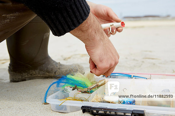 Schnappschuss einer männlichen Hand  die am Strand einen Angelhaken vorbereitet