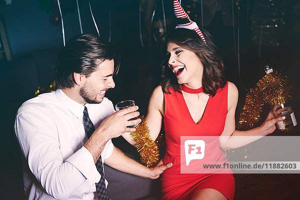 Mann und Frau sitzen auf einer Party zusammen  halten Getränke in der Hand  lachen