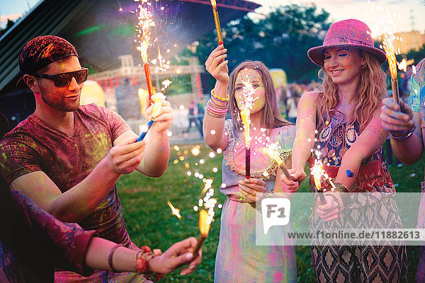 Young adults covered in coloured chalk powder holding sparklers at festival