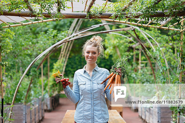 Frau im Garten hält Karottenbündel lächelnd