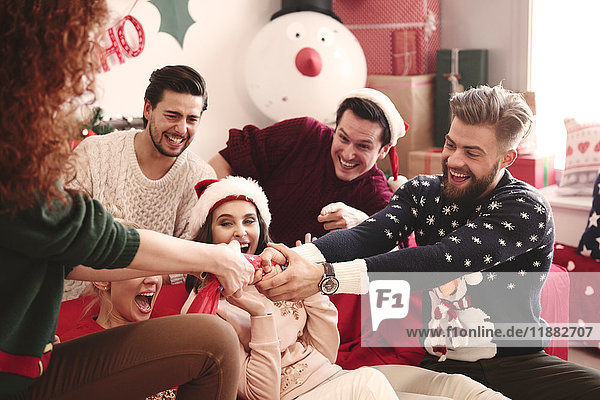 Young adult friends pulling christmas crackers on sofa at christmas party