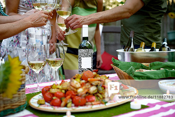 Personengruppe beim Gartenfest  Weingläser halten  Toast ausbringen  Essen auf dem Servierteller im Vordergrund  Mittelteil
