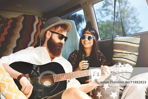 Young boho couple playing acoustic guitar in recreational van