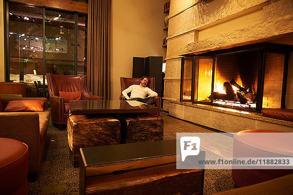 Porträt eines Mannes  der sich in einem Sessel am Kaminfeuer in einer Hotel-Lounge entspannt  Aspen  Colorado  USA