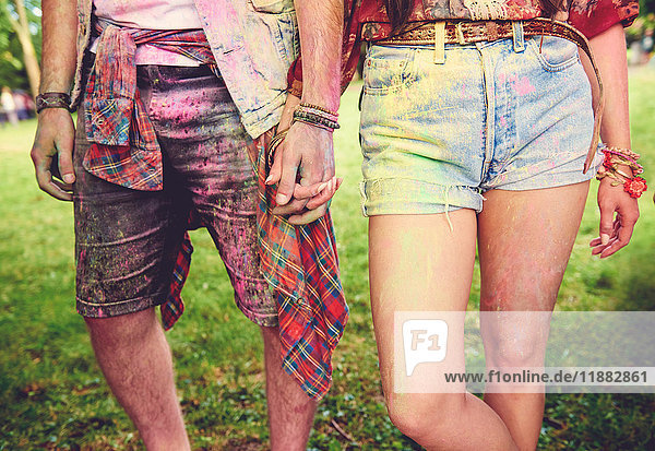 Waist down view of young couple covered in coloured chalk powder at festival