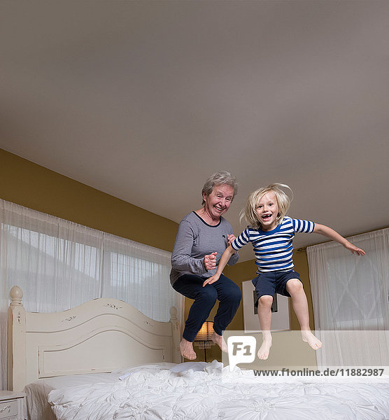 Grandson and grandmother jumping on bed