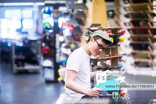Junger männlicher Verkäufer beim Reparieren eines Skateboards an der Ladentheke eines Skateboard-Ladens