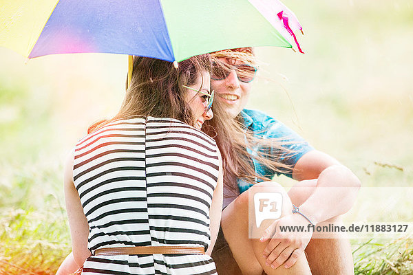 Junges Paar mit Regenschirm entspannt sich auf dem Feld
