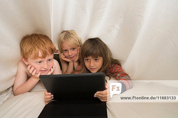 Kinder liegen im Bett und schauen auf das digitale Tablett