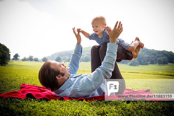 Mid adult man lying on back balancing baby son in rural field