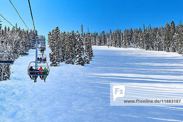 Rückansicht von Skifahrern auf einem Skilift  die sich in einer verschneiten Landschaft fortbewegen  Aspen  Colorado  USA
