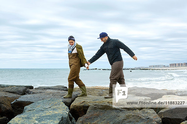 Young sea fishing couple stepping over beach rocks