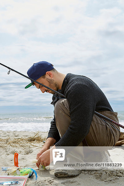 Hockender junger Mann bereitet Angelhaken am Strand vor