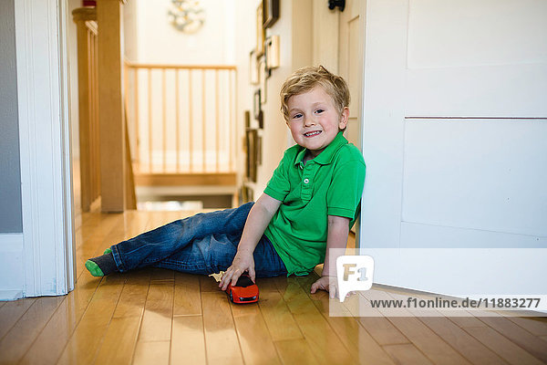 Porträt eines Jungen mit auf dem Boden sitzendem Spielzeugauto