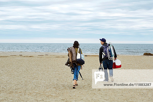Rear view of young couple carrying sea fishing equipment on beach