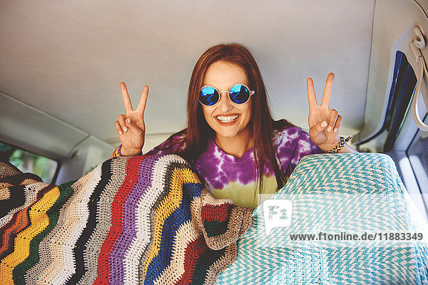 Portrait of young boho woman making peace sign in recreational van