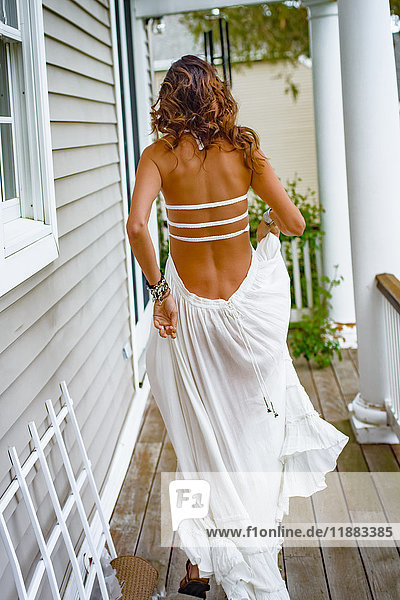 Rückansicht einer Frau in langem weißen Kleid beim Verlassen der Hausveranda
