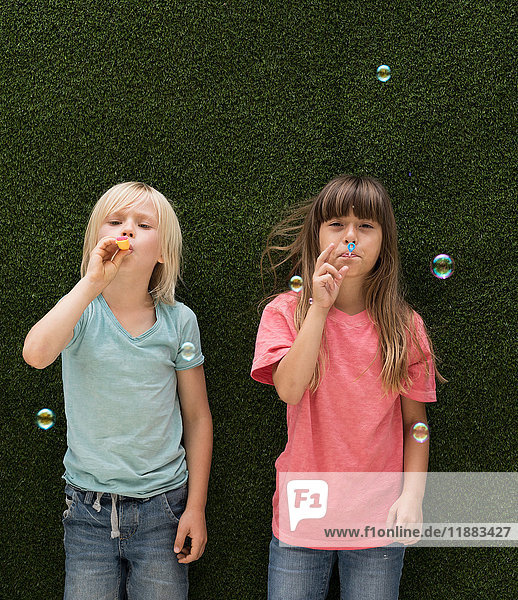 Children in front of artificial grass wall blowing bubbles