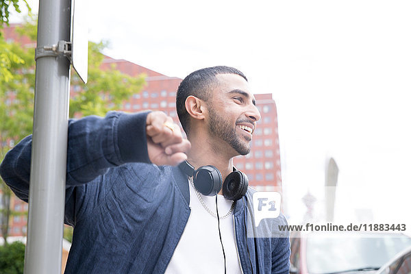 Young man leaning against lamppost  headphones around neck  smiling