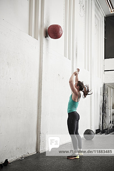 Woman throwing fitness ball against wall in cross training gym