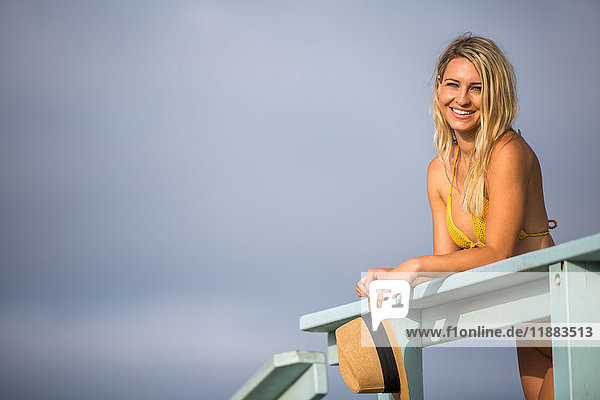 Porträt einer jungen Frau in Bikini-Oberteil  die sich an den Balkon einer Strandhütte lehnt  Santa Monica  Kalifornien  USA