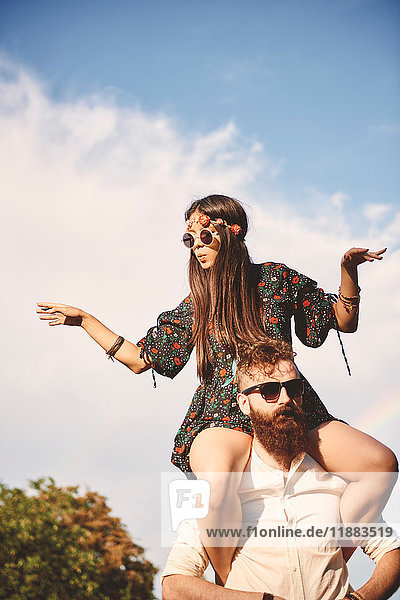 Young boho woman dancing on boyfriend's shoulders at festival