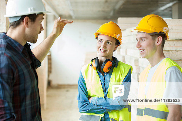 Drei Personen stehen auf der Baustelle  tragen Schutzhelme und diskutieren