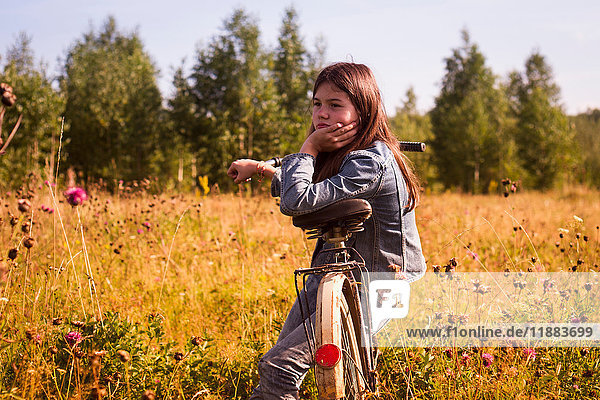 Teenager-Mädchen sitzt auf Fahrrad in langem Grasfeld