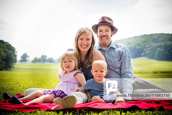Portrait of mid adult couple sitting on picnic blanket with daughter and baby son