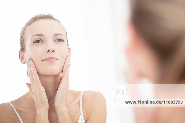 Junge Frau schaut in den Spiegel und trägt Feuchtigkeitscreme auf das Gesicht auf