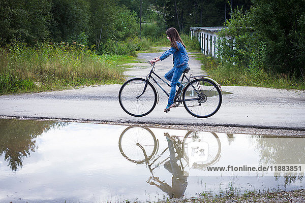Teenage girl cycling along rural road past puddle
