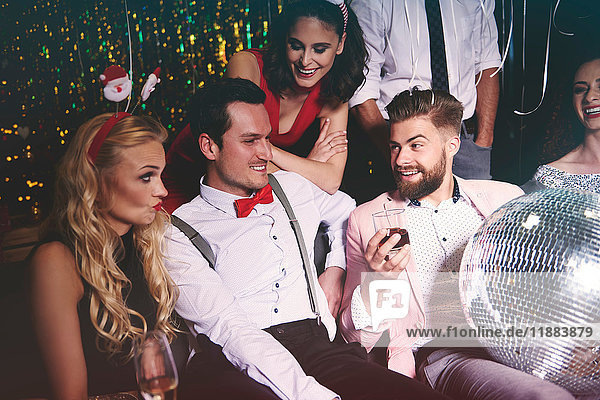 Gruppe von Freunden sitzt auf Party zusammen  Mann hält Discokugel auf dem Schoß