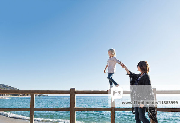 Young boy walking along fence  holding mother's hand  Laguna Beach  California  United States  North America