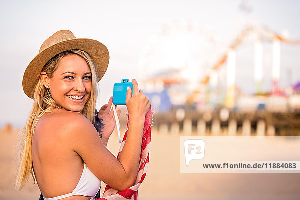 Porträt einer jungen Frau in Bikini-Oberteil beim Fotografieren eines Vergnügungsparks am Strand  Santa Monica  Kalifornien  USA