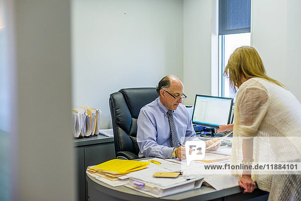 Senior man discussing paperwork with office worker at office desk