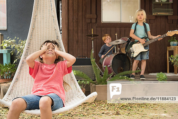 Girl in hanging chair hands on head and children playing guitar and drums in band